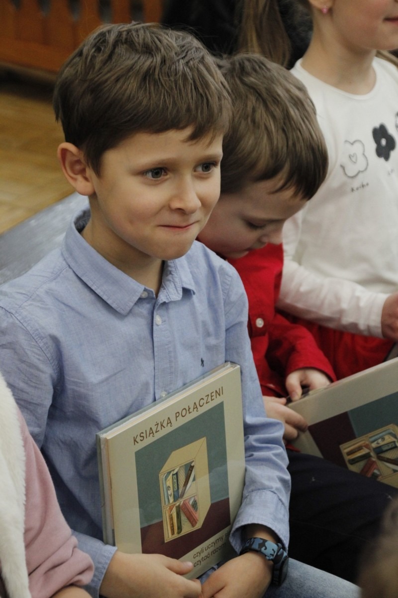 Chłopczyk w niebieskiej koszuli trzyma książkę pt. "Pierwsze abecadło"