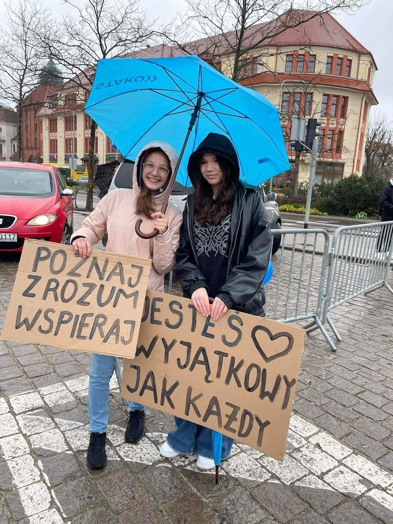 Uczennice na placu z niebieską parasolką i plakatem 1