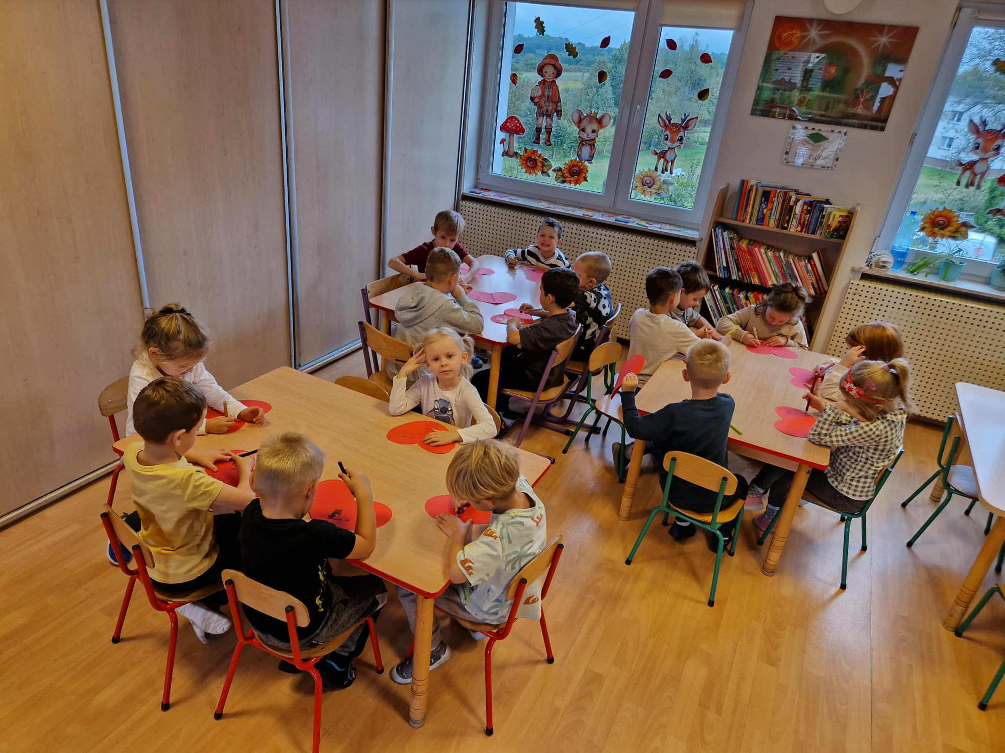 dzieci siedzą przy stoliku i rysują na sercach minki