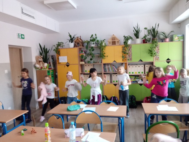 Dzieci stoją w klasie w rzędzie i wyglądają tak, jakby się poruszały.


