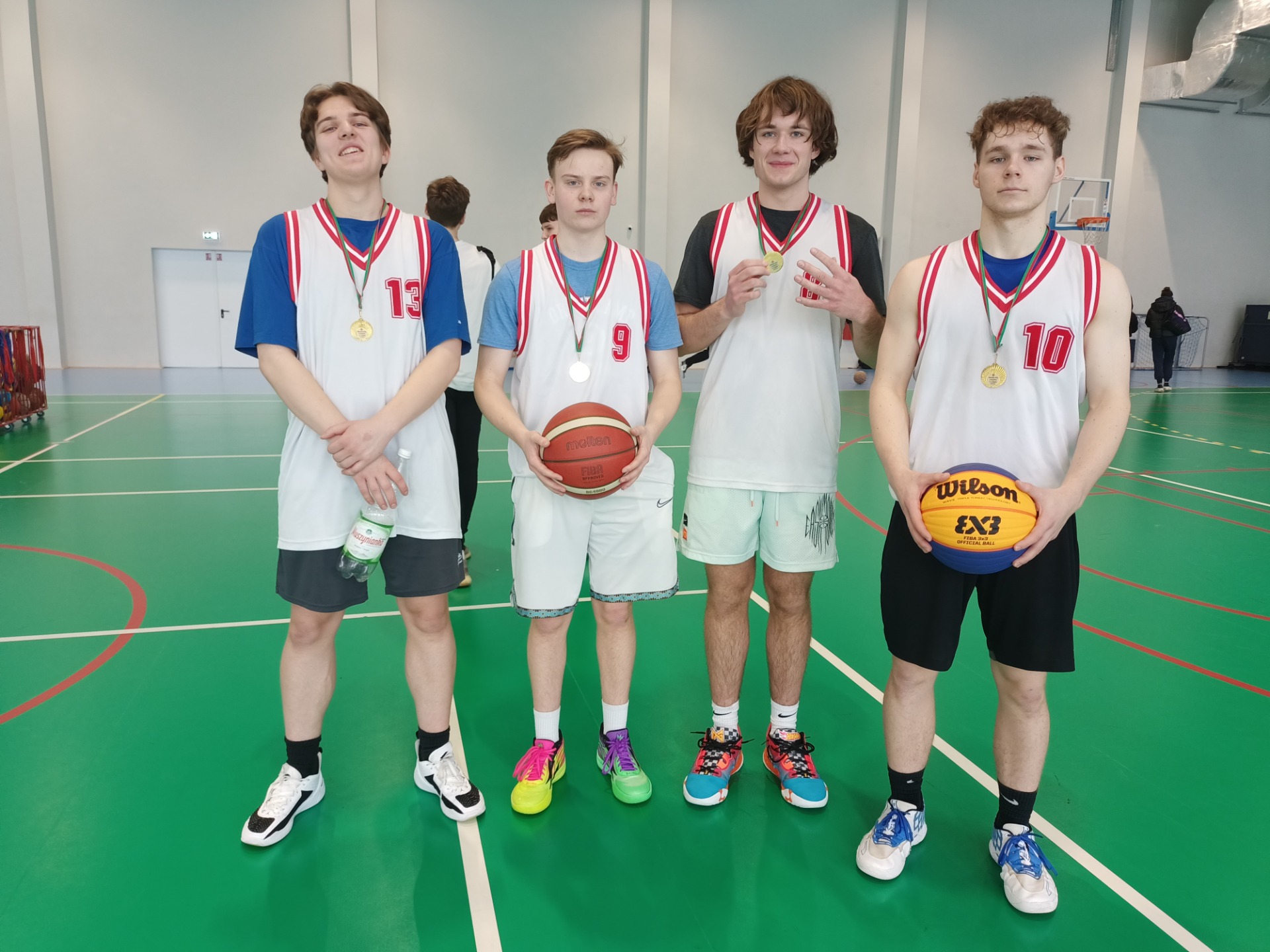 Drużyna koszykówki z medalami - czterech uczniów stoi na hali sportowej. 
