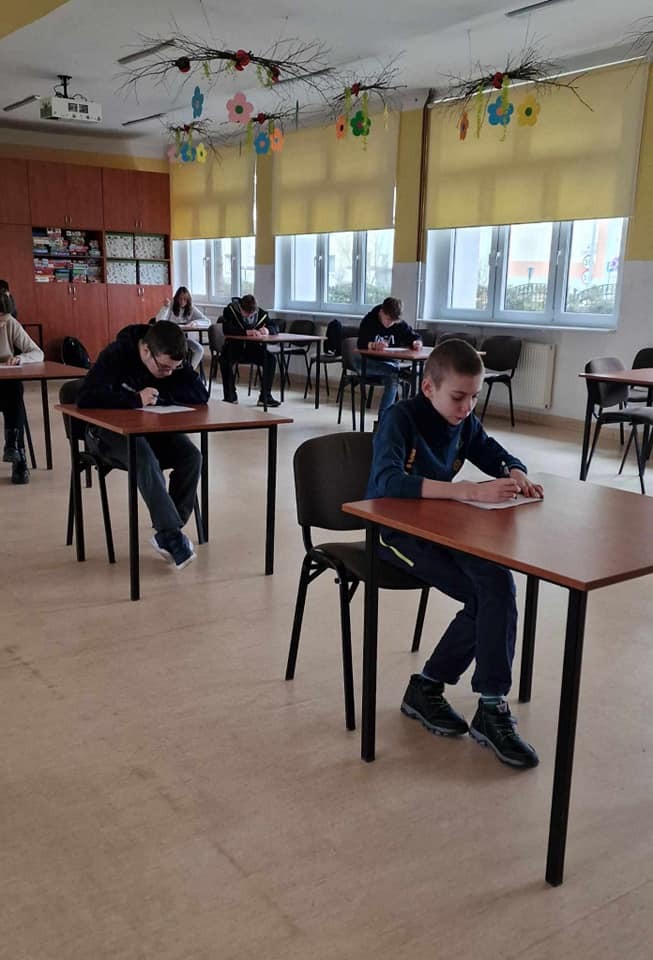 Uczniowie rozwiązują test o Januszu Korczaku, siedzą w lawkach, każdy w osobnej. Na zdjęciu ok 5 uczniów