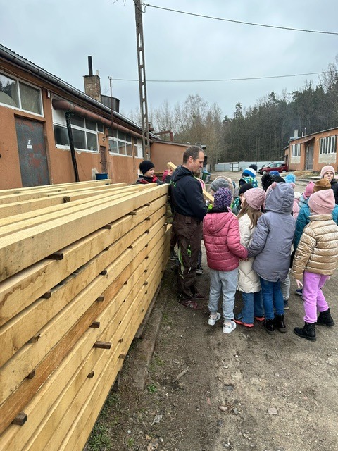 2-13 uczniów wraz z Panem Kamilem przygląda się dla drewna złożonego na zewnątrz zakładu
