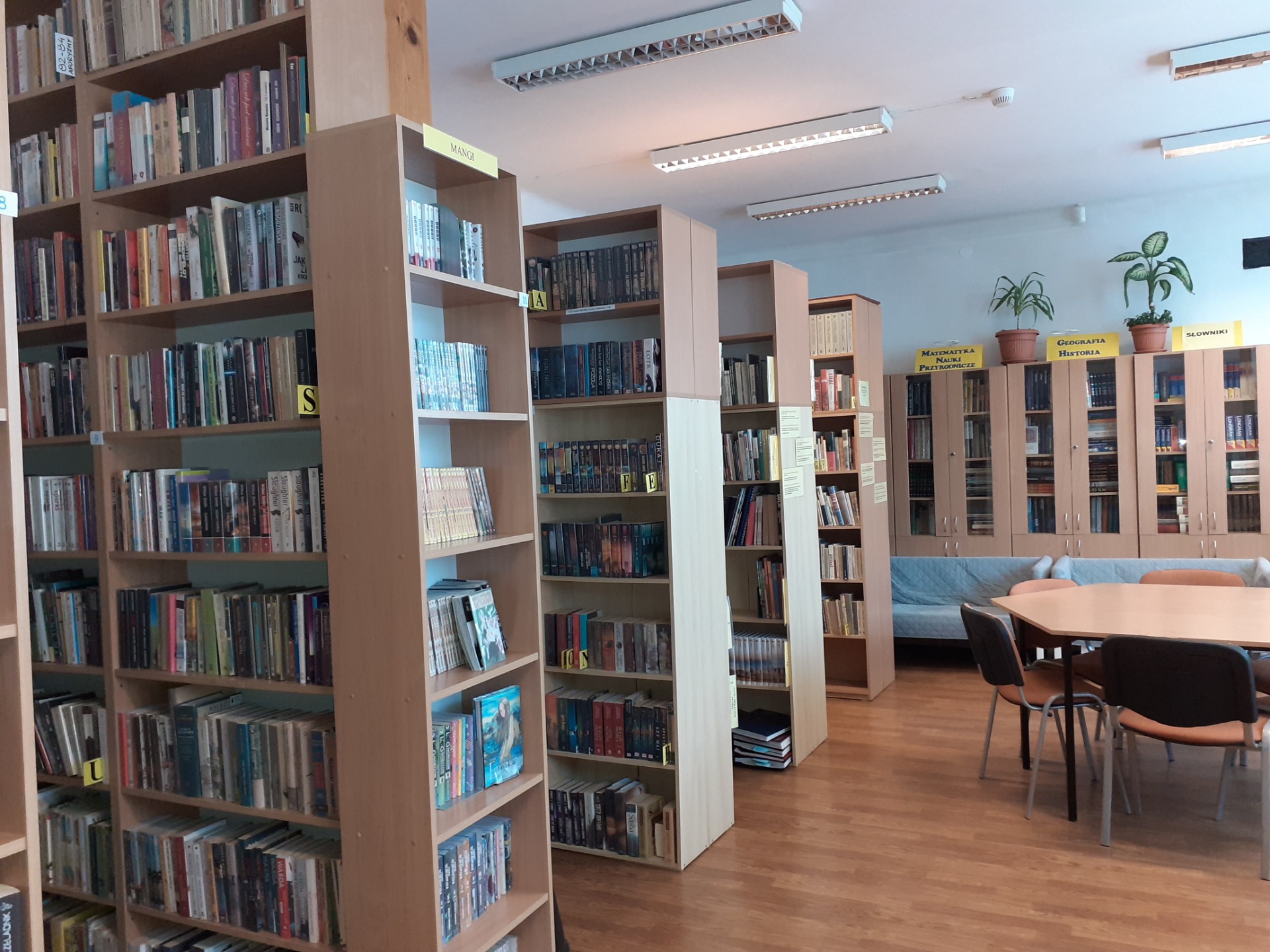 Zdjęcie przedstawia bibliotekę szkolną: regały z książkami , na środku pomieszczania stolik za nim kanapa.