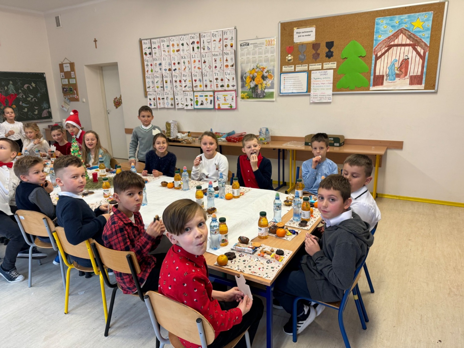 Dzieci siedzą przy stole, na stole biały obrus, ciasteczka, owoce.
