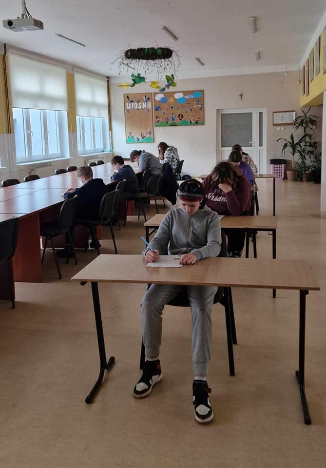Uczniowie rozwiązują test o Januszu Korczaku, siedzą w lawkach, każdy w osobnej. Na zdjęciu ok 10 uczniów