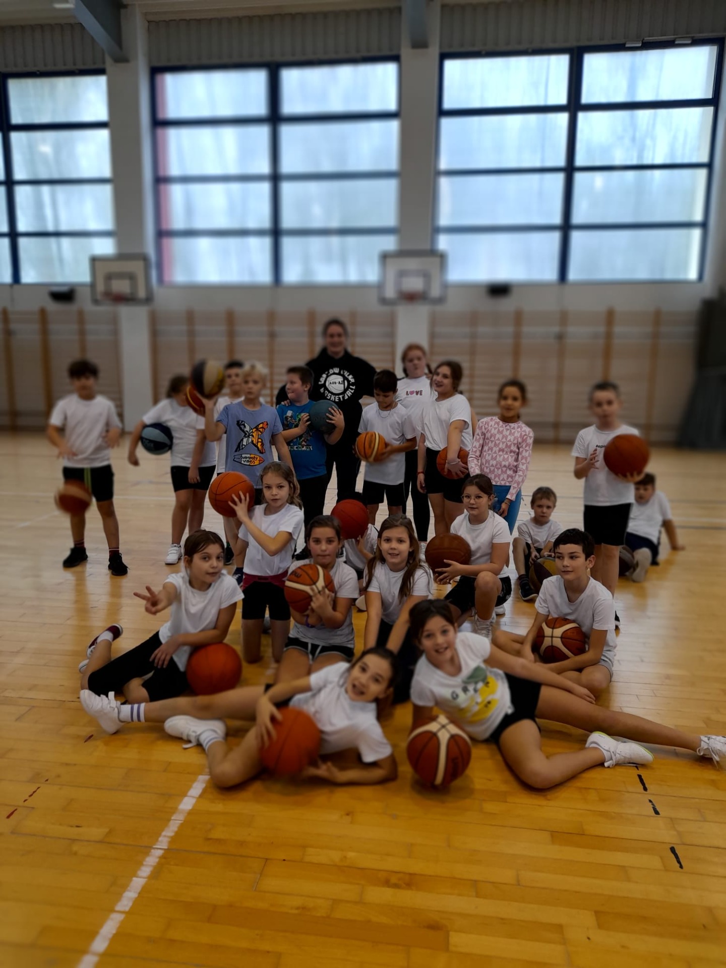 Grupa dzieci z trenerem koszykówki pozuje do zdjęcia na hali sportowej