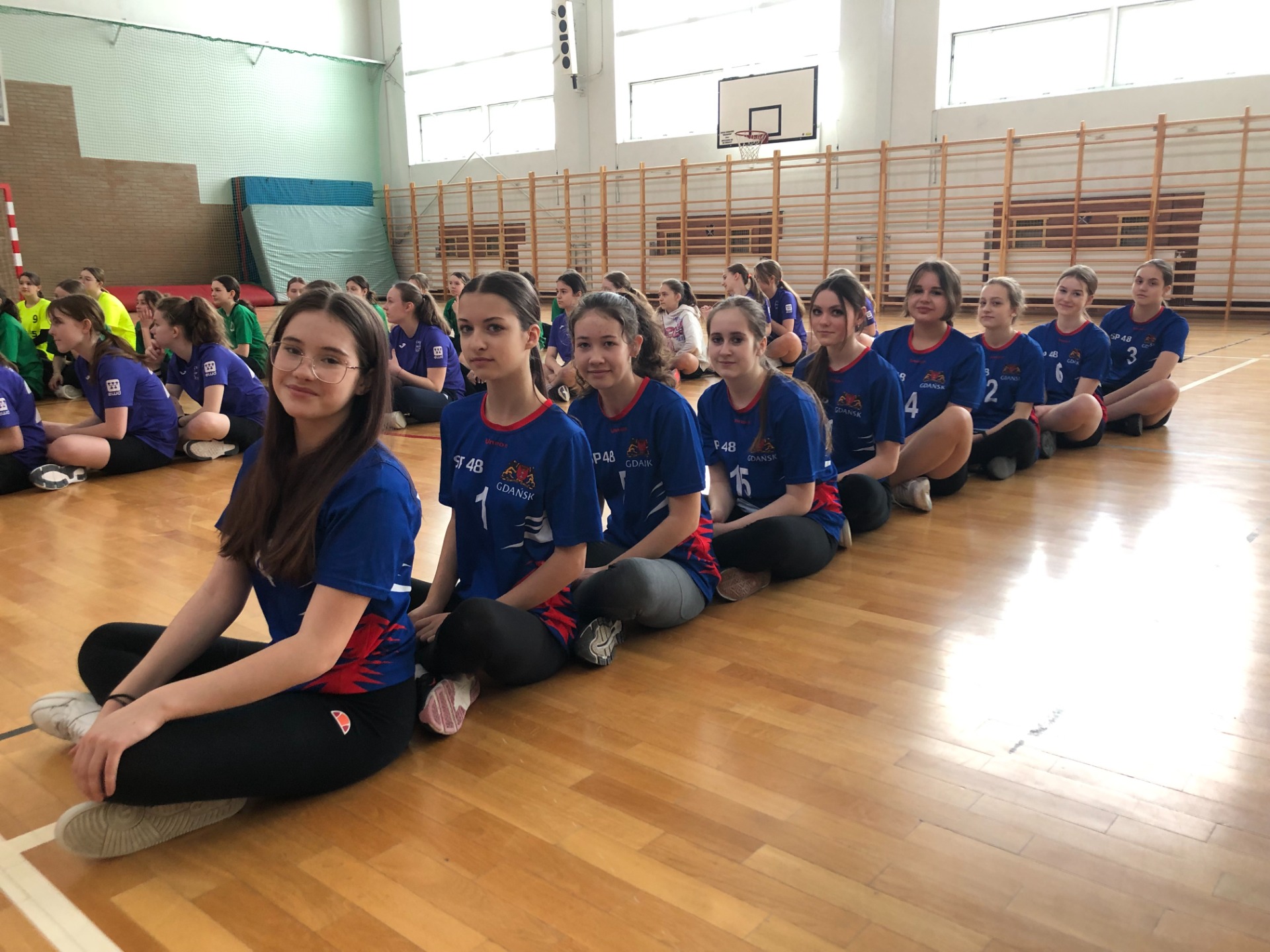 Dziewczynki w niebiesiech strojach w sali gimnastycznej.