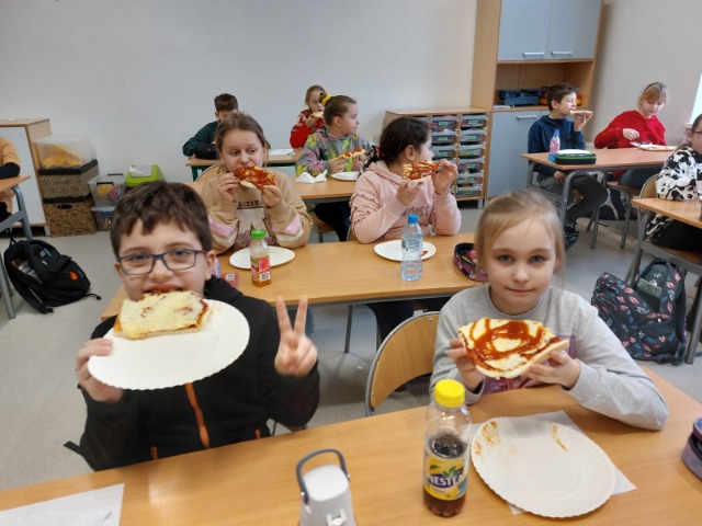Uczniowie jedzący pizzę.
