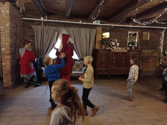 4 dzieci tańczy z Mikołajem. Z lewej strony stoi elf Mikołaja.