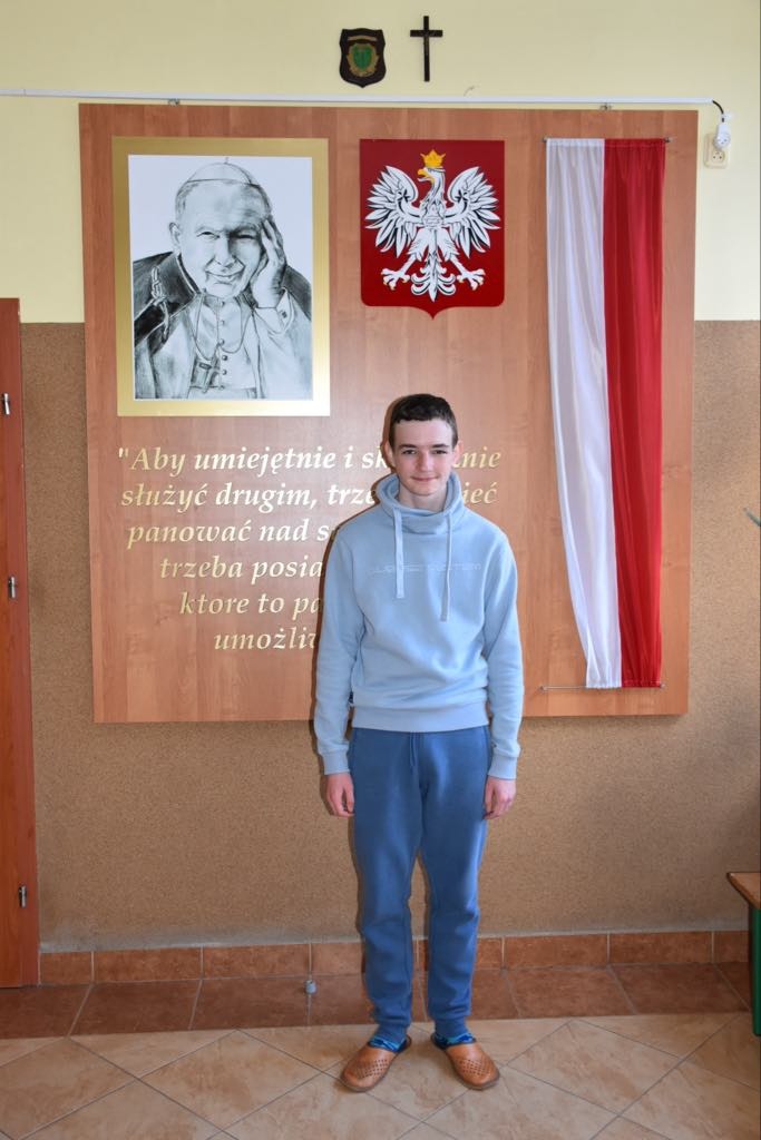Janek na tle tablicy pamiątkowej ze Zdjęciem Jana Pawła II.