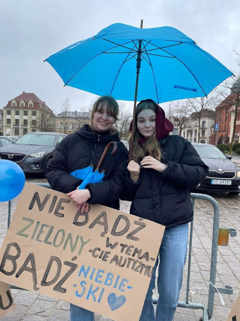 Uczennice na placu z niebieską parasolką i plakatem 2