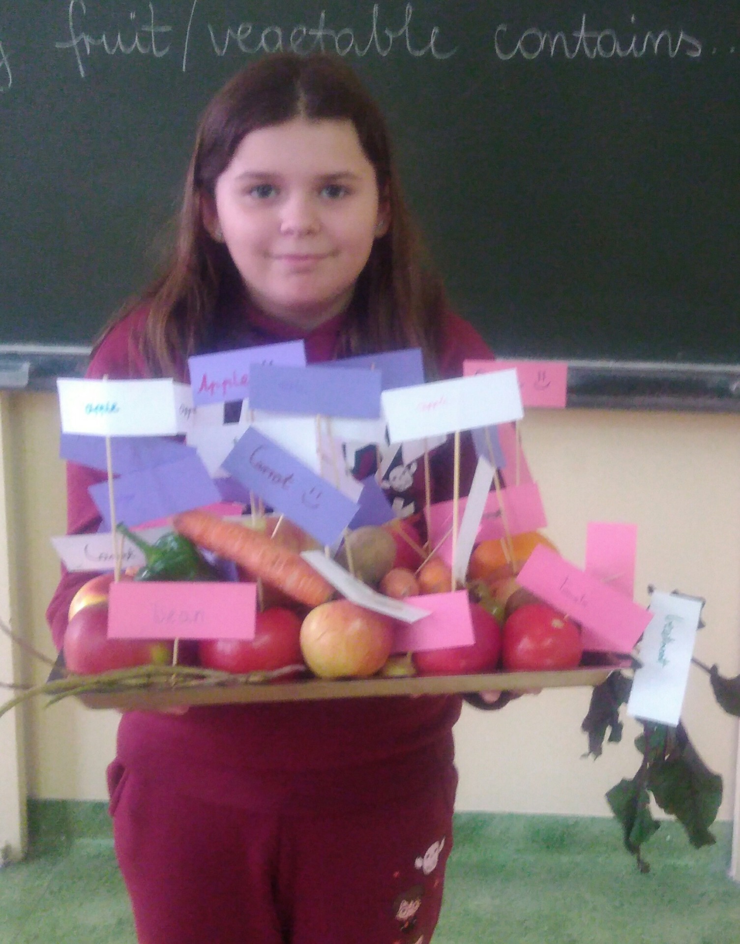 Uczennica z tacą etykietowanych owoców i warzyw.