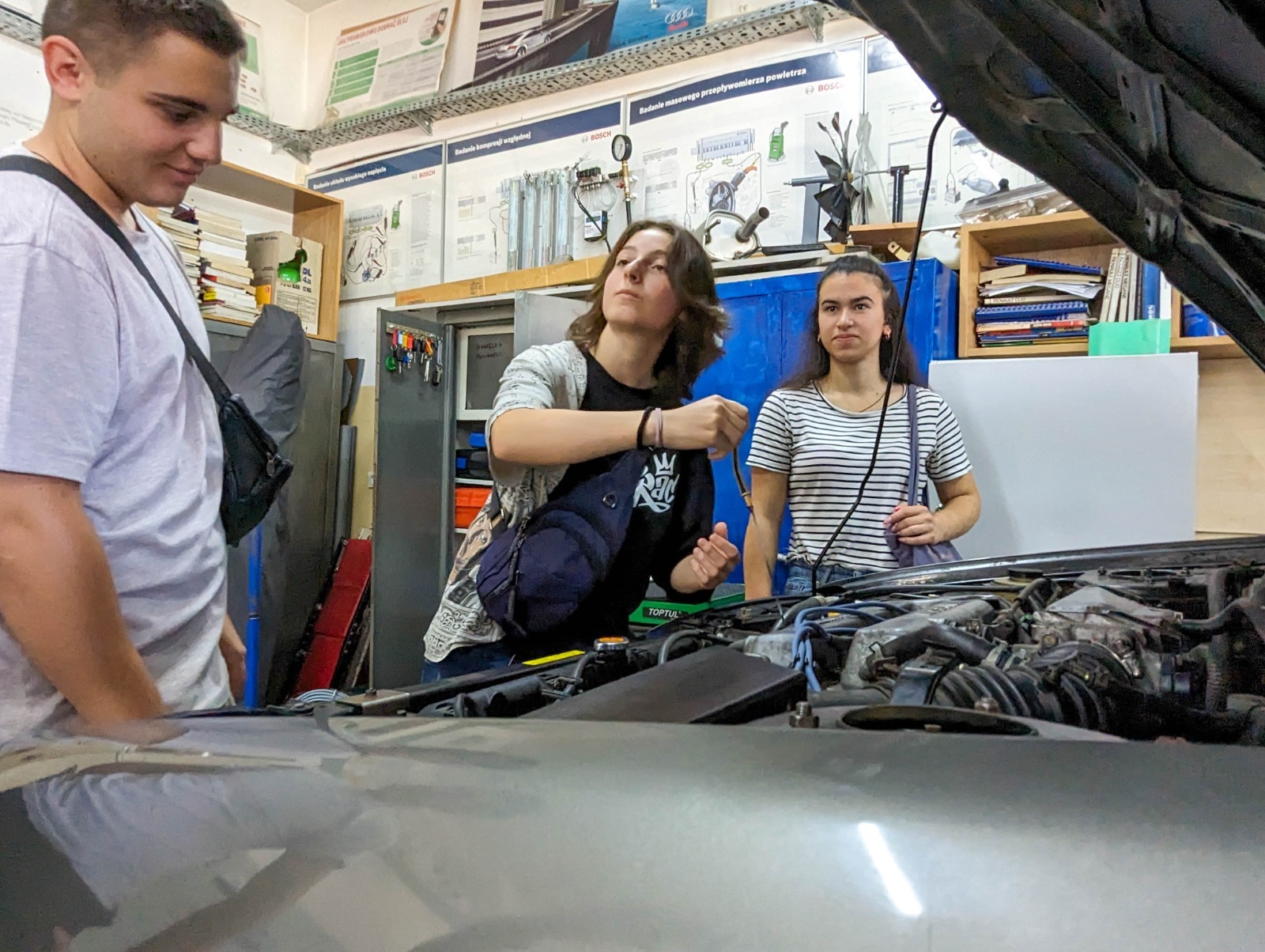 Wizyta w pracowni samochodowej - uczniowie stoją przed otwartą maską samochodu. 